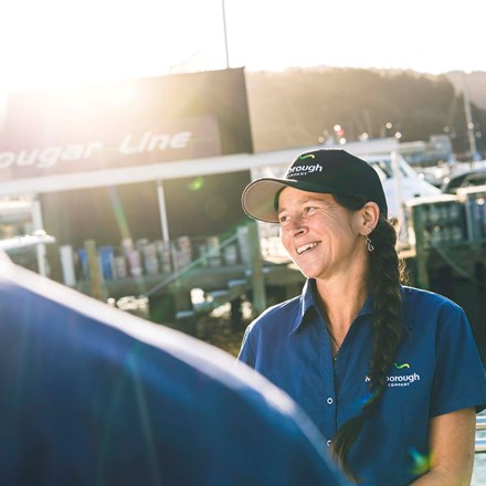 Smiling staff member in blue uniform on a boat in Picton Marina, in the Marlborough Sounds at the top of New Zealand's South Island
