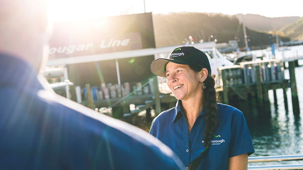 Smiling staff member in blue uniform on a boat in Picton Marina, in the Marlborough Sounds at the top of New Zealand's South Island