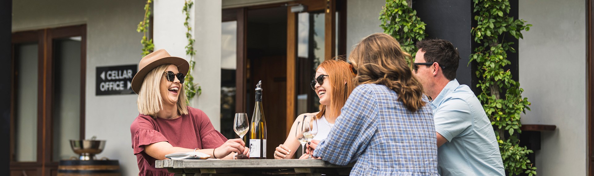 Four people sitting outdoors at a winery cellar door drinking wine on a wine tour Marlborough near Blenheim, at the top of New Zealand's South Island