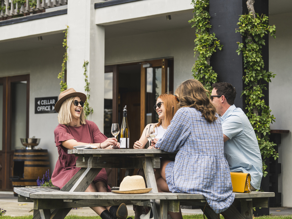 Four people sitting outdoors at a winery cellar door drinking wine on a wine tour Marlborough near Blenheim, at the top of New Zealand's South Island