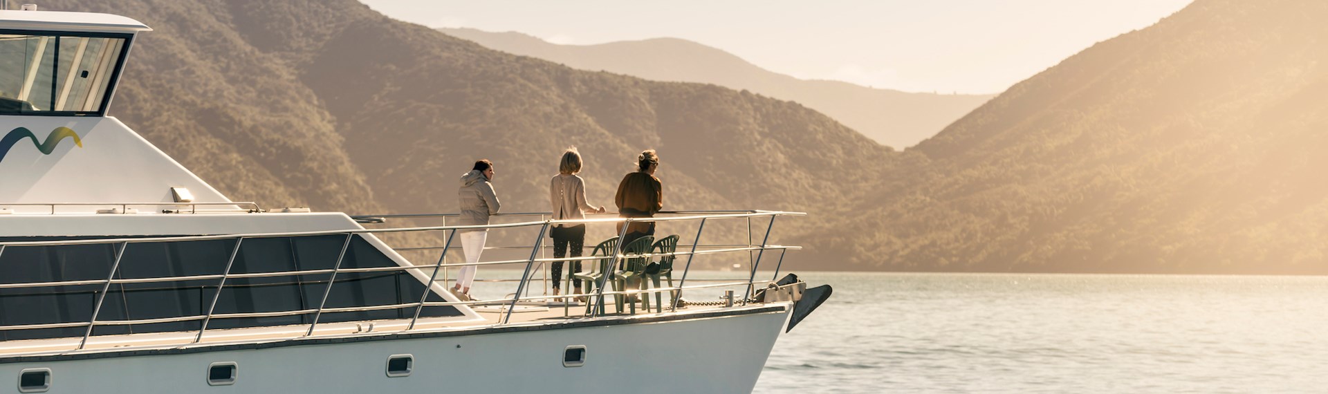 Cruising the Marlborough Sounds at the top of New Zealand's South Island, people view the sun set over the bush clad hills from the bow of MV Odyssea