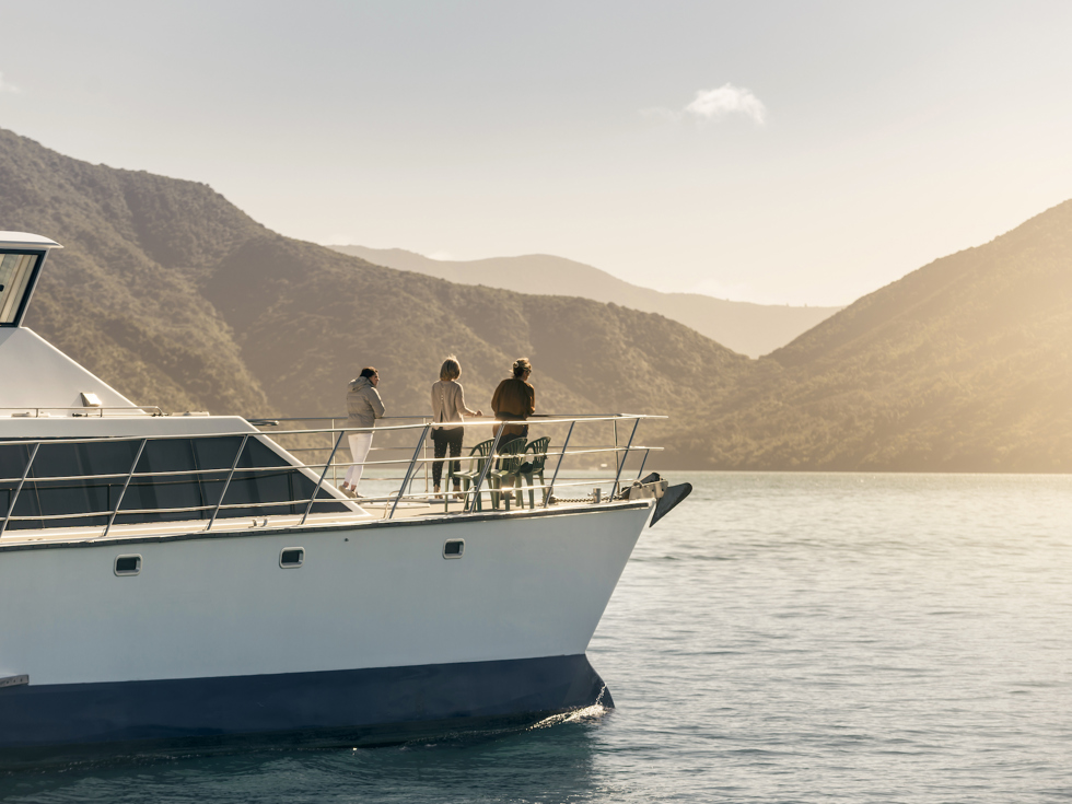 Cruising the Marlborough Sounds at the top of New Zealand's South Island, people view the sun set over the bush clad hills from the bow of MV Odyssea