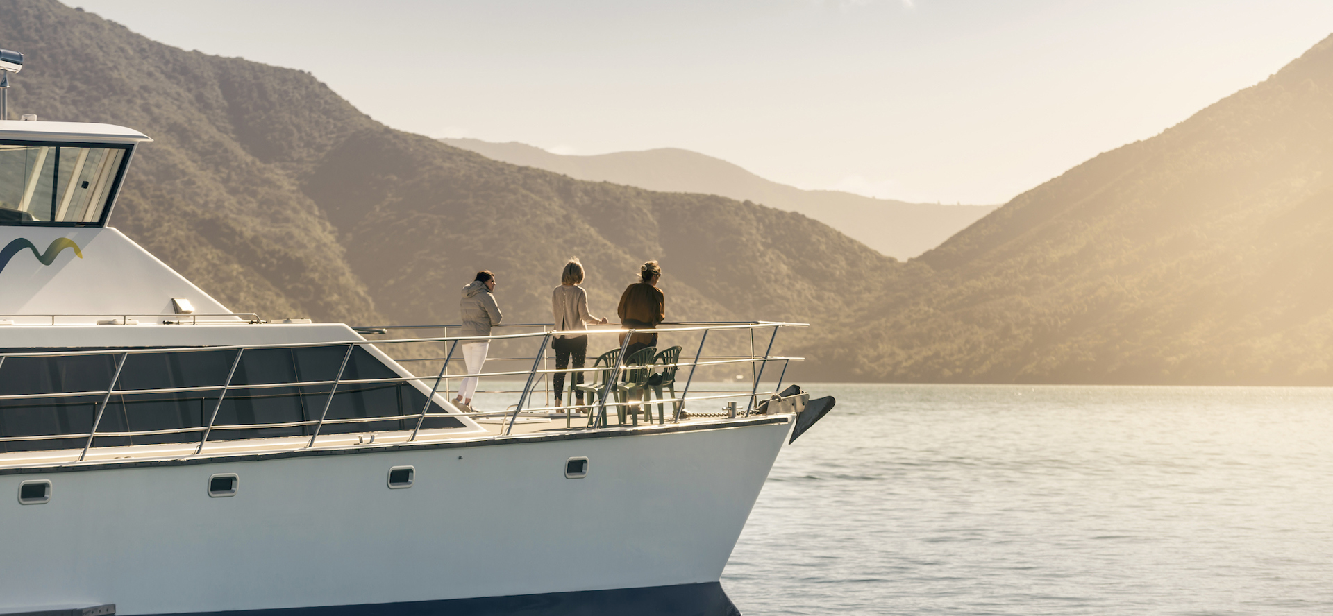Cruising the Marlborough Sounds at the top of New Zealand's South Island, people view the sun set over the bush clad hills from the bow of MV Odyssea