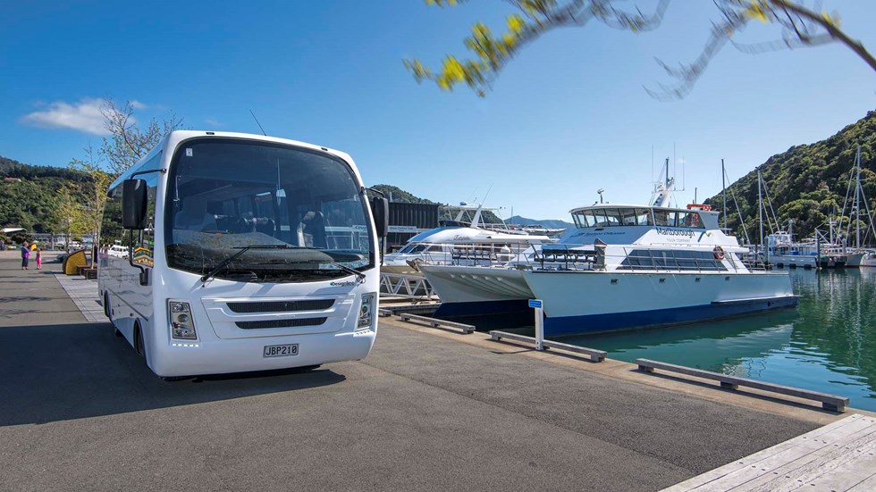 White bus parked next to large white launch at Picton Marina ready for tours and transfers with Marlborough Tour Co, in Marlborough at the top of New Zealand's South Island.