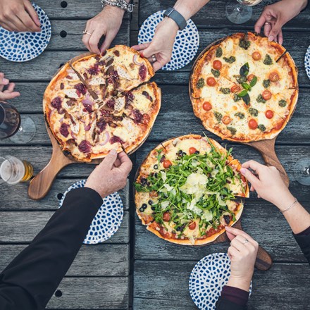 A group of friends share three hot stone baked pizzas and drinks from the Boatshed Cafe and Bar at Punga Cove located in the Marlborough Sounds of New Zealand's South Island