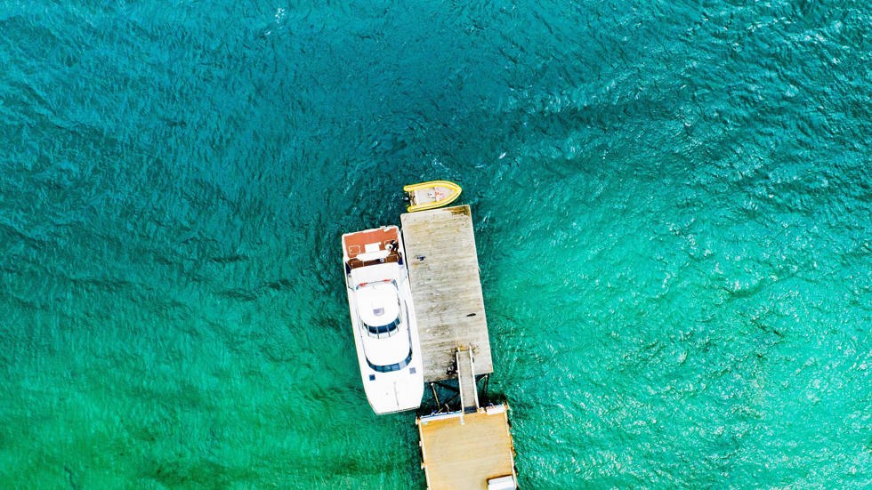 Aerial view of Marlborough Tour Company's MV Mantra docked at Furneaux Lodge surrounded by blue/green sea, at the top of New Zealand's South Island. 