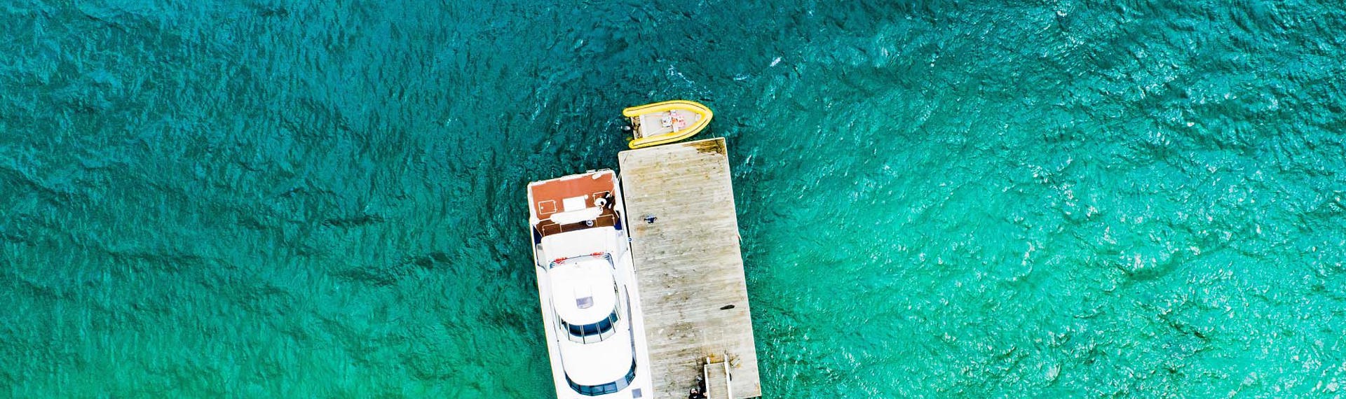 Aerial view of Marlborough Tour Company's MV Mantra docked at Furneaux Lodge surrounded by blue/green sea, at the top of New Zealand's South Island. 