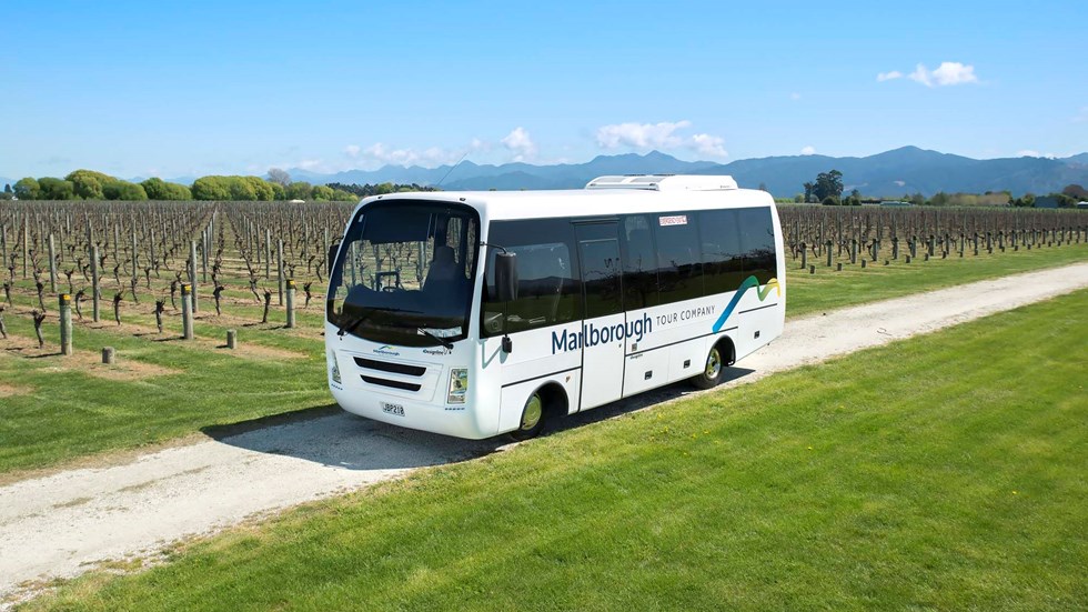 Small white coach on road amongst vineyards on a Marlborough Tour Co wine tour, near Blenheim in Marlborough at the top of New Zealand's South Island.