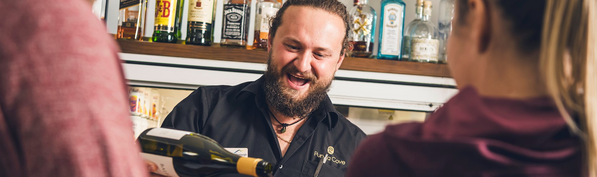 A friendly bartender pours Pinot Noir into glasses for customers at the Boatshed Cafe and Bar at Punga Cove - choose from a great range of local craft beer, wine , cocktails, soft drinks and expresso coffee.