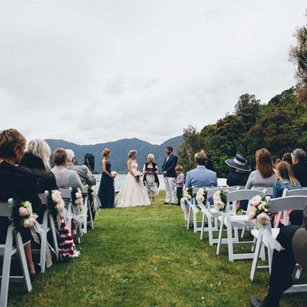 Bride and Groom say their vows at a Punga Cove wedding on the front lawn with seated guests in the Marlborough Sounds of New Zealand