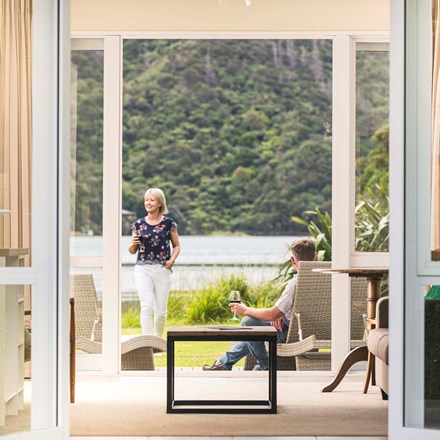 A couple enjoy glasses of wine on their private Endeavour Suite deck at Furneaux Lodge in the Marlborough Sounds at the top of New Zealand's South Island.