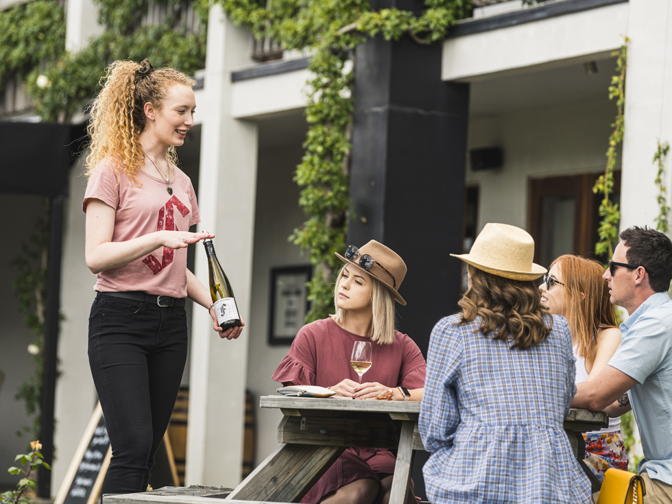 Four people on a wine tour enjoy being taken through a guided wine tasting at a winery cellar door in Marlborough, at the top of New Zealand's South Island