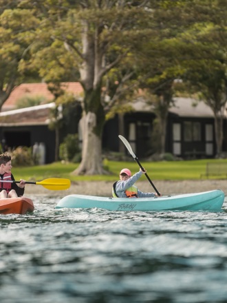 Two boys paddle kayaks in front of Furneaux Lodge in New Zealand's Marlborough Sounds.