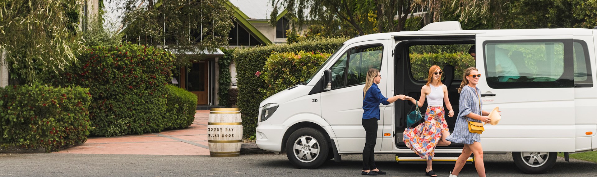 Two women are helped out of a van by a Marlborough Tour Co staff member on a wine tour at a winery cellar door in Marlborough, at the top of New Zealand's South Island