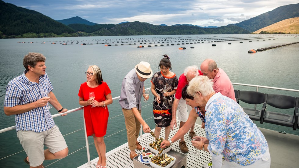A group enjoys Greenshell mussels and wine onboard MV Spirit on a Marlborough Tour Company cruise in the Marlborough Sounds, at the top of New Zealand's South Island