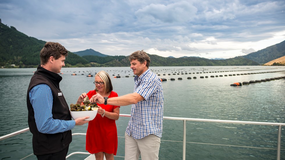 A couple taste steamed fresh Greenshell mussels, served at the source on a Seafood Odyssea cruise in New Zealand's Marlborough Sounds from Picton.