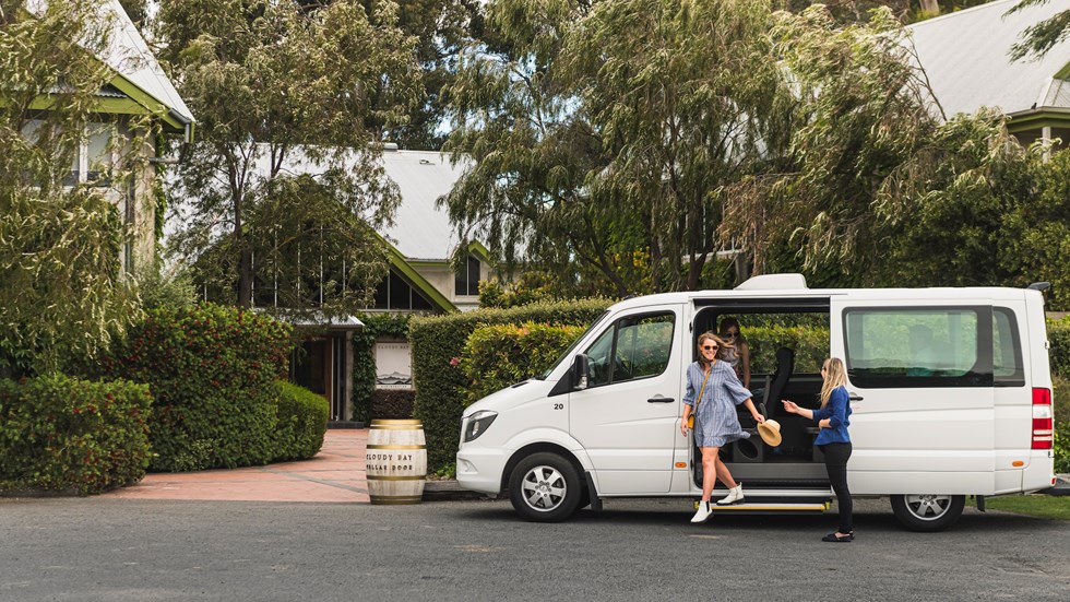 Two women exit a van helped by a Marlborough Tour Co staff member at a winery cellar door in Marlborough near Blenheim, at the top of New Zealand's South Island