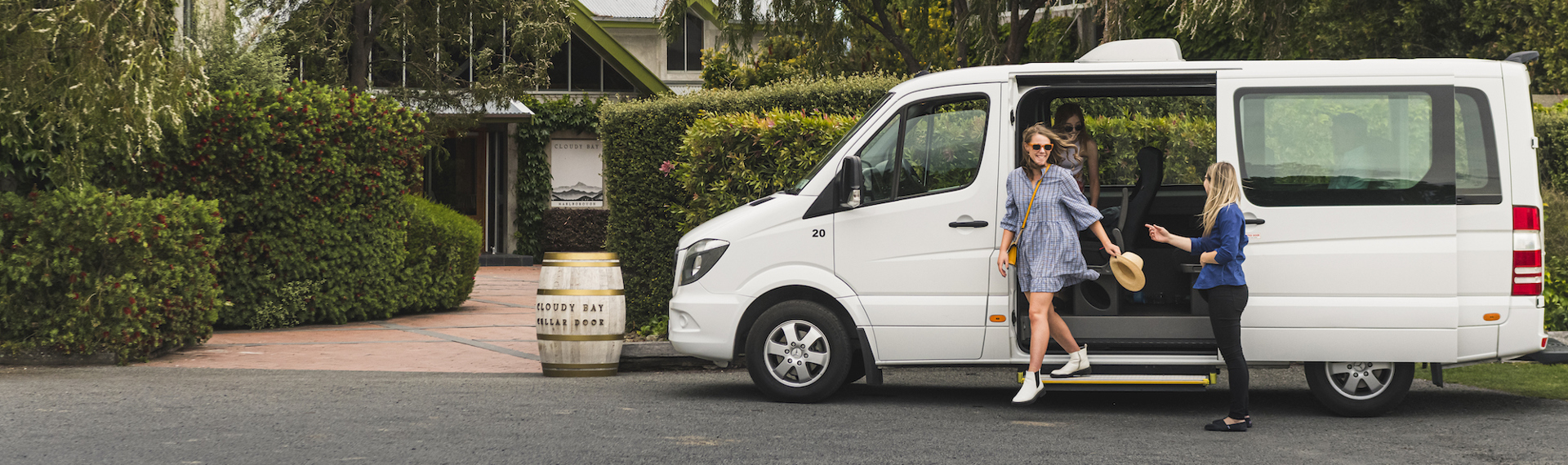 Two women exit a van helped by a Marlborough Tour Co staff member at a winery cellar door in Marlborough near Blenheim, at the top of New Zealand's South Island