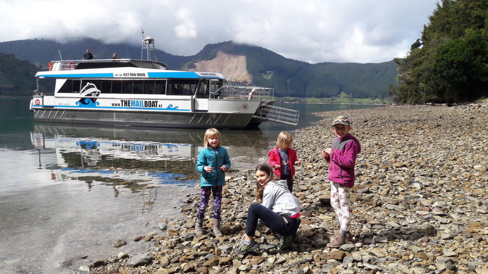 Four children on a rocky beach with Pelorus Mail Boat docked behind.