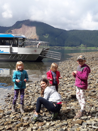 Four children on a rocky beach with Pelorus Mail Boat docked behind.