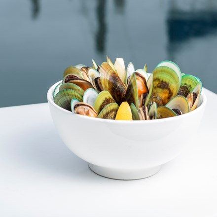 A bowl of freshly steamed Greenshell mussels on a boat with water behind, at Havelock Marina at the top of New Zealand's South Island.