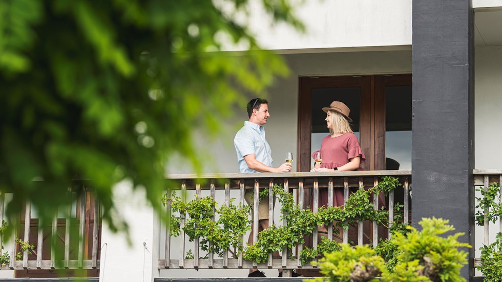 A couple enjoys glasses of wine on a balcony at a winery cellar door on a wine tour in Marlborough, at the top of New Zealand's South Island